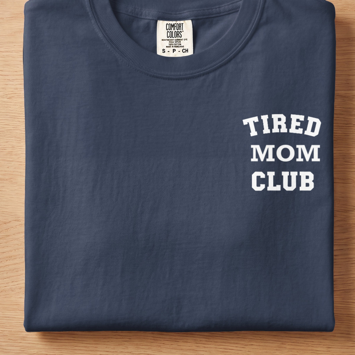 Dark navy t-shirt with white text "TIRED MOM CLUB" on the right chest.