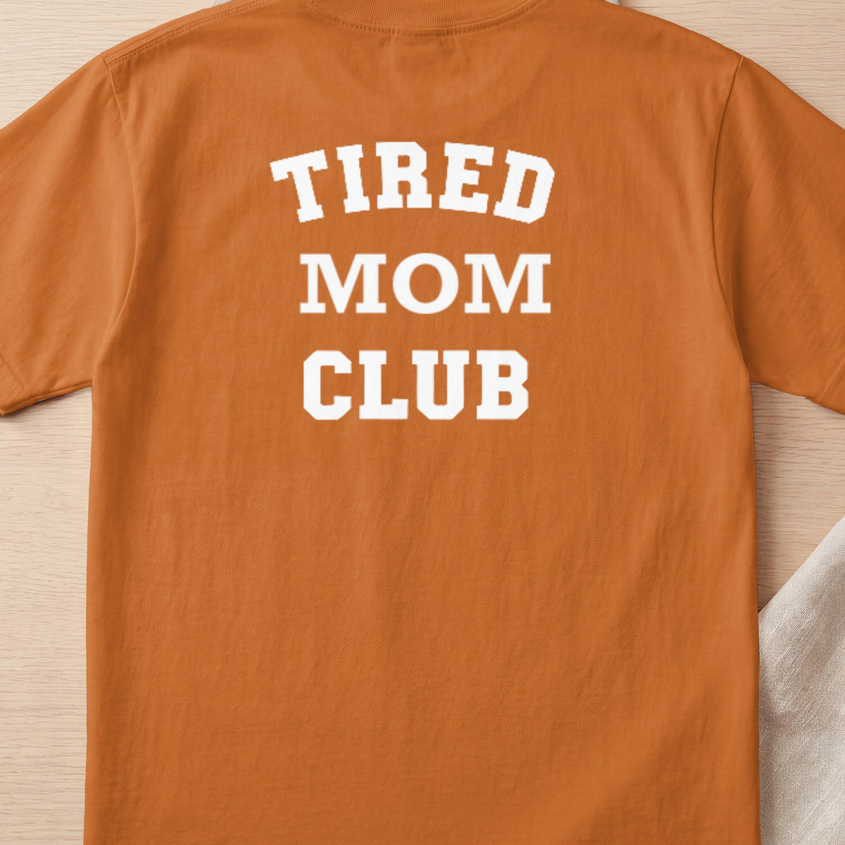 Orange t-shirt with white text "TIRED MOM CLUB" across the back.