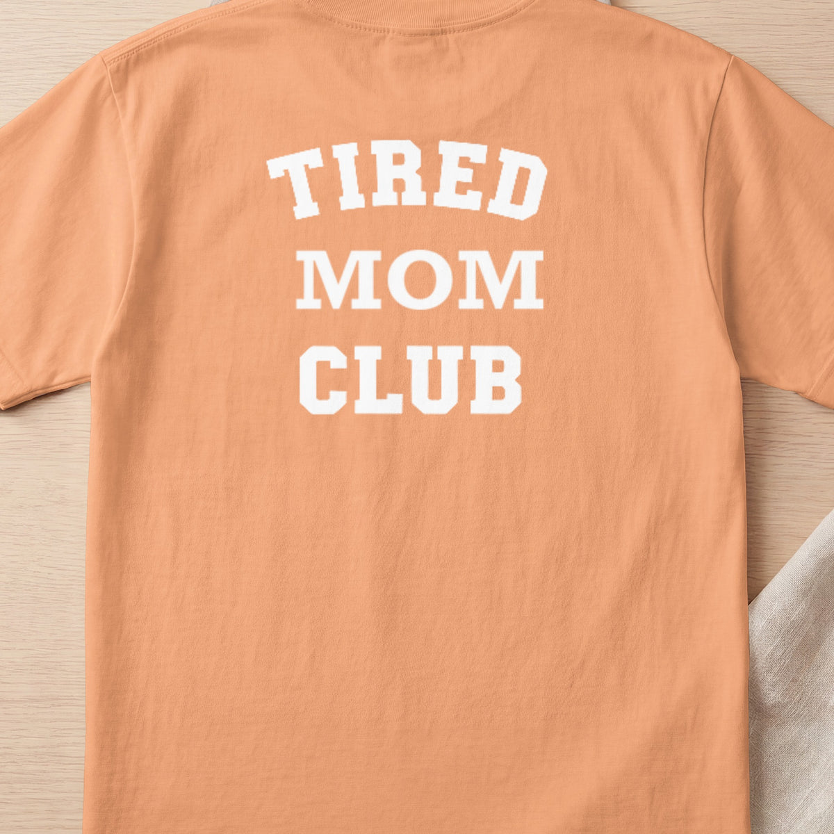 Peach t-shirt with white text reading "TIRED MOM CLUB".