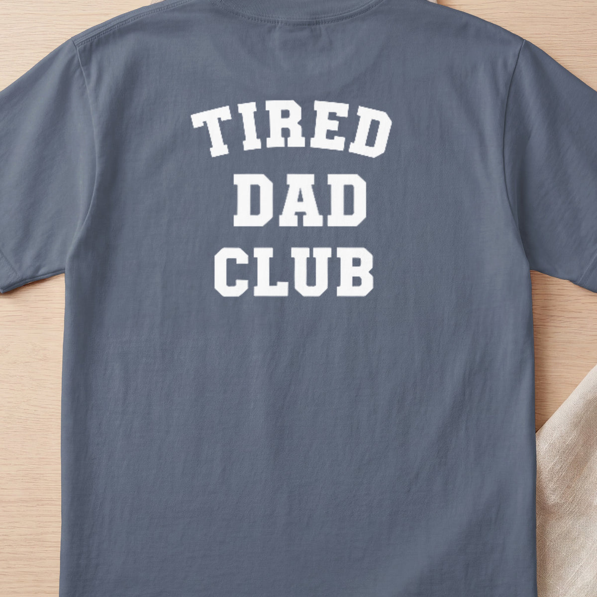 Slate blue t-shirt with white collegiate text reading "TIRED DAD CLUB".