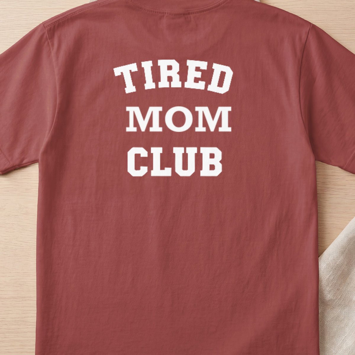 Rust colored t-shirt with white text "TIRED MOM CLUB" on back.