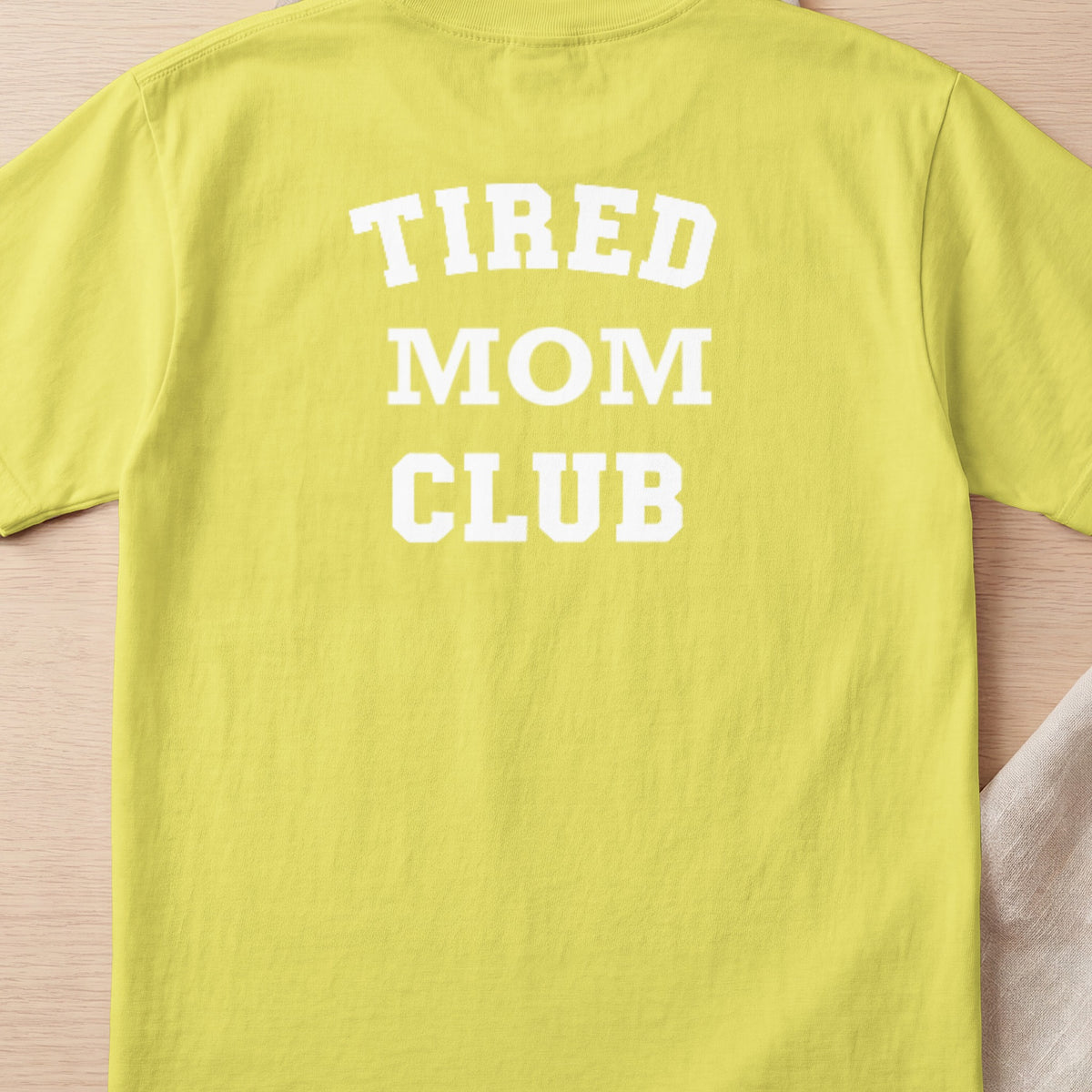 Yellow t-shirt with white text "TIRED MOM CLUB" in block letters.